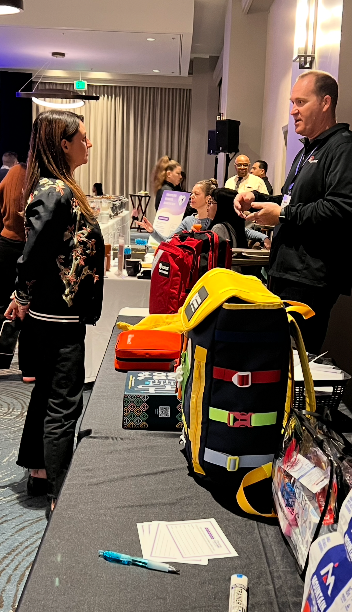 People interacting with display of bags and products at an event.