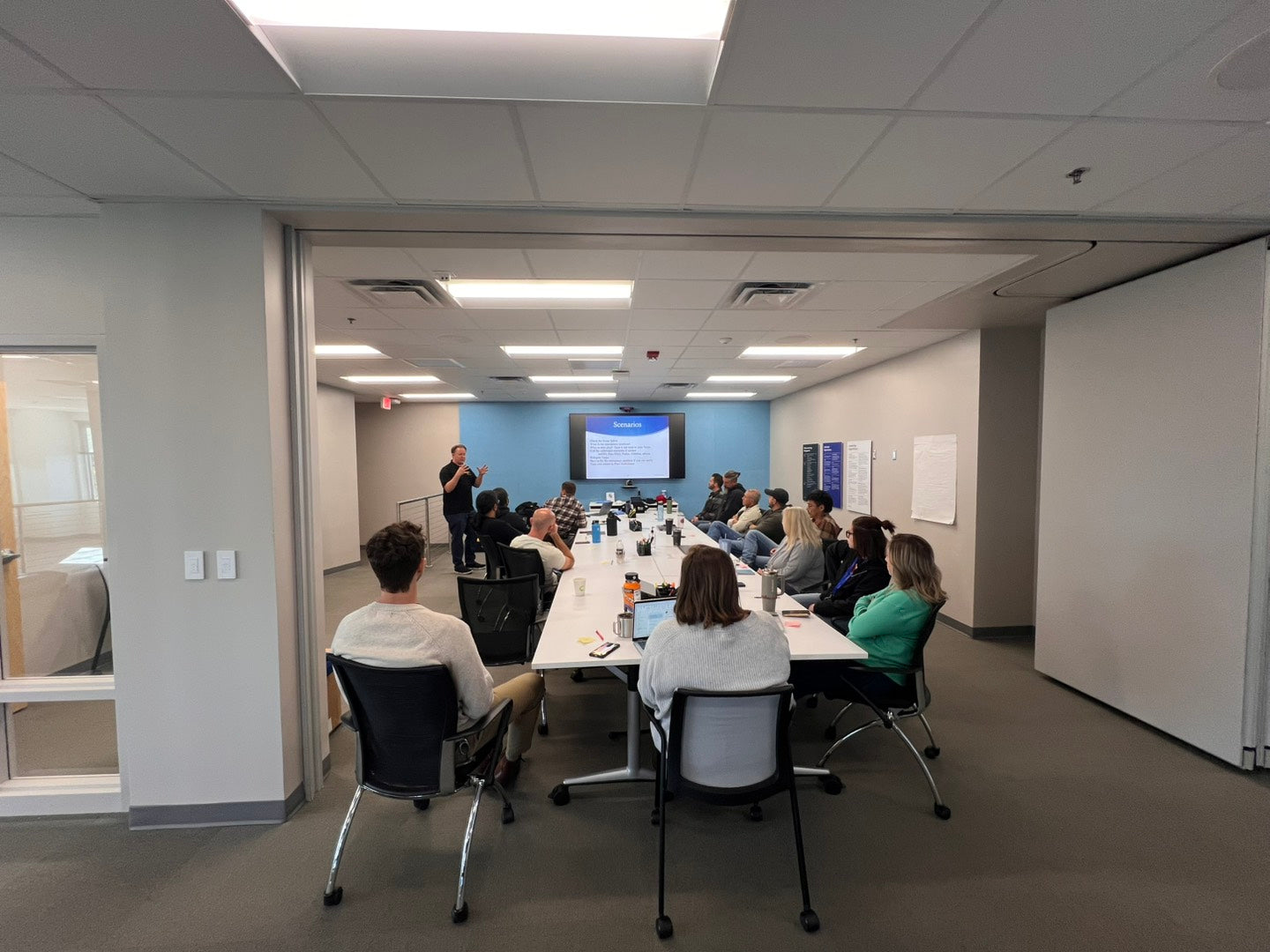 Group of people in a conference room with a presenter at a table.