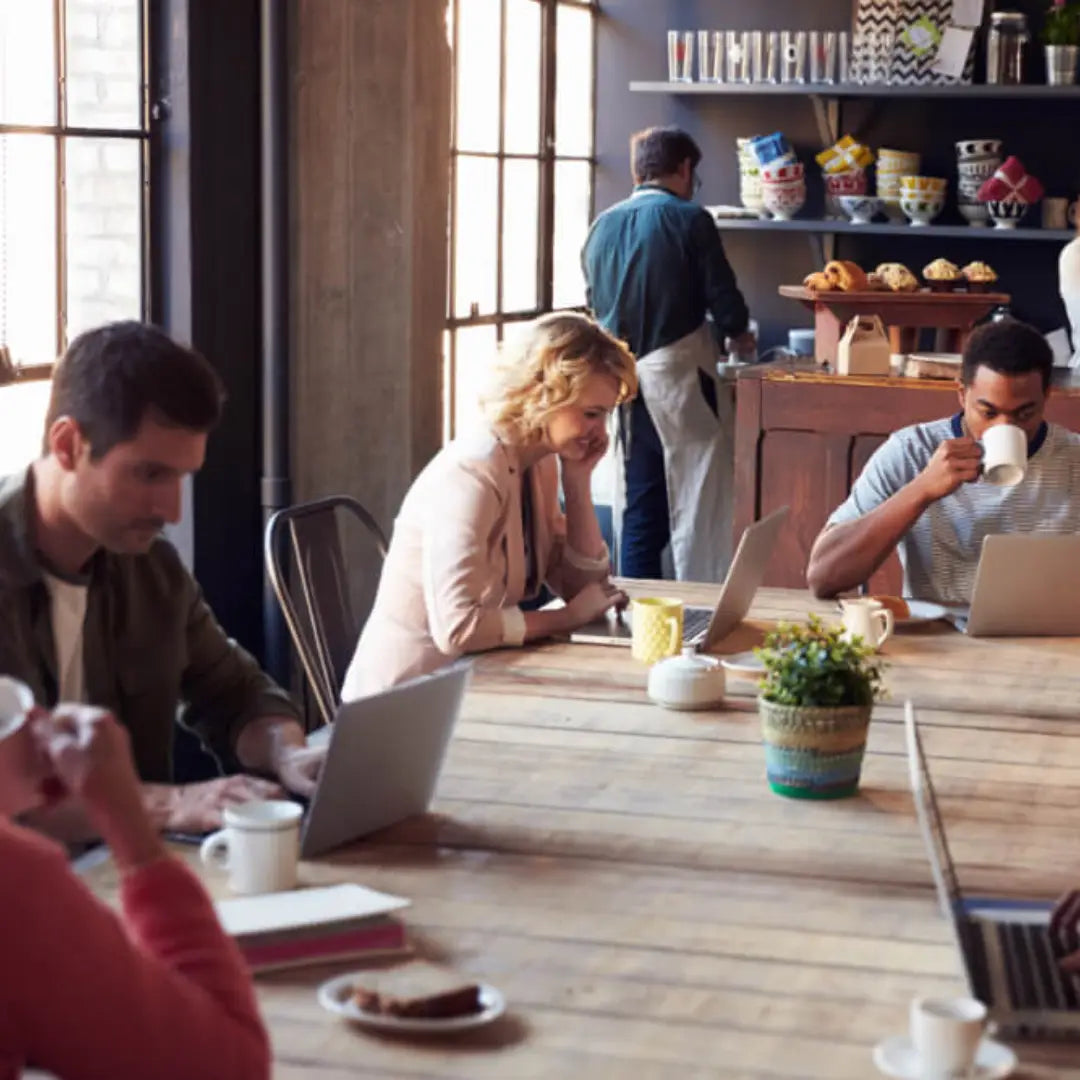 People working on laptops at a wooden table in a casual office setting.