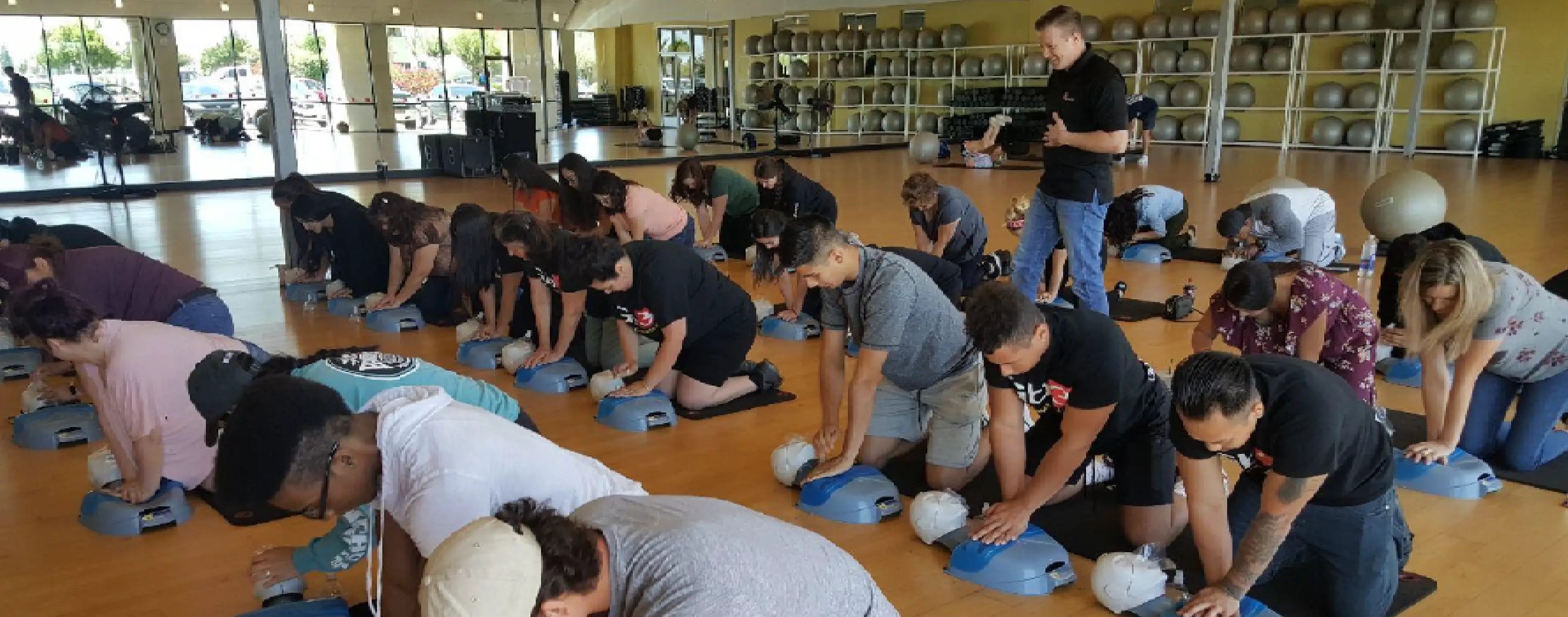 Group of people practicing CPR on mannequins in a classroom setting.