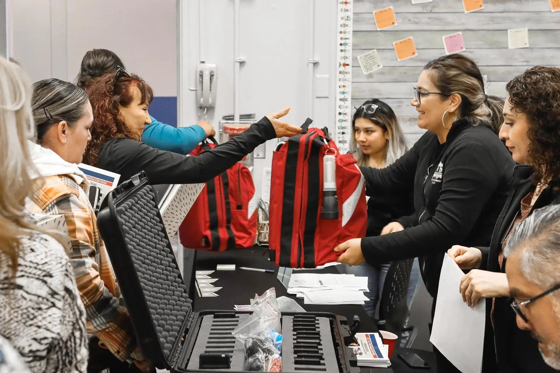 Group of people gathered around a table with bags and documents in an indoor setting.