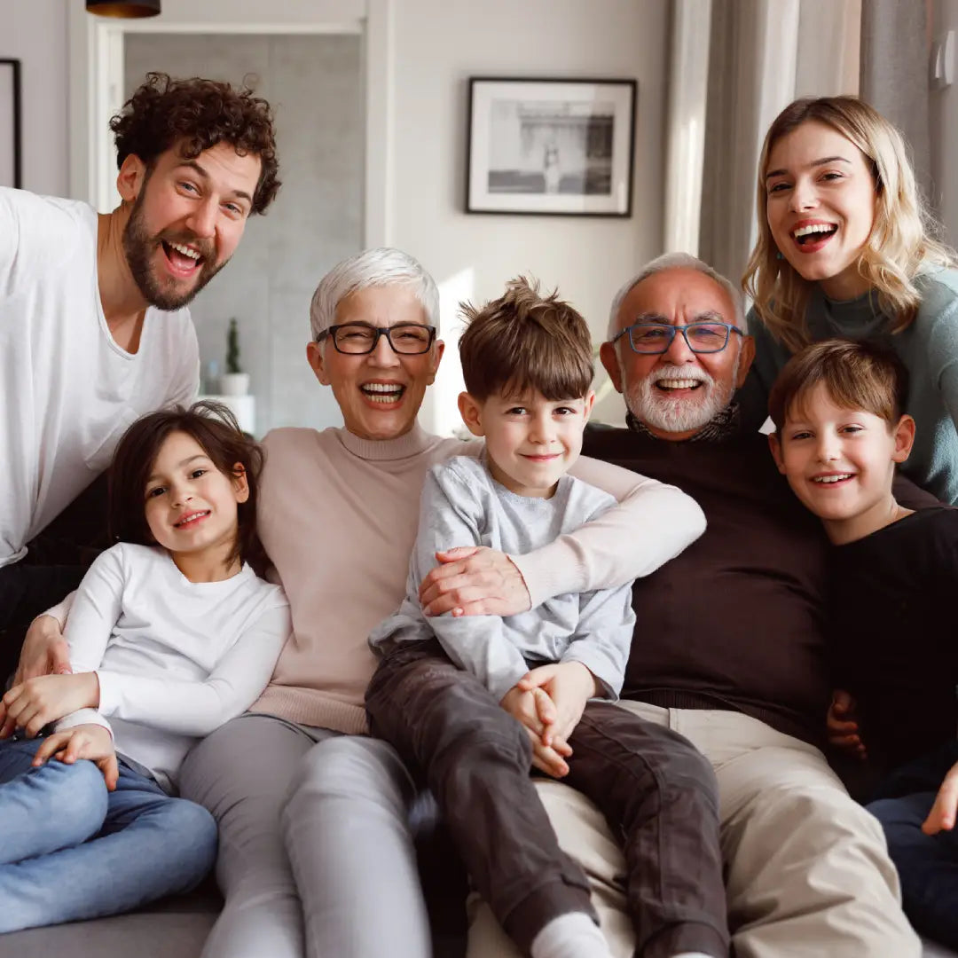 Family of six, including adults and children, sitting together on a couch in a living room.