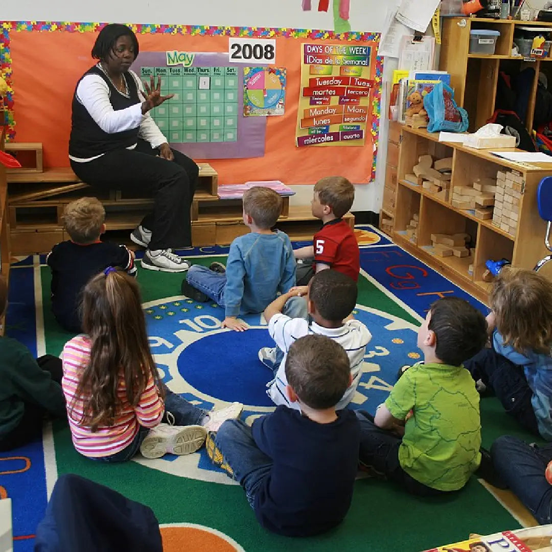 Teacher with students in a classroom setting with educational posters and toys.