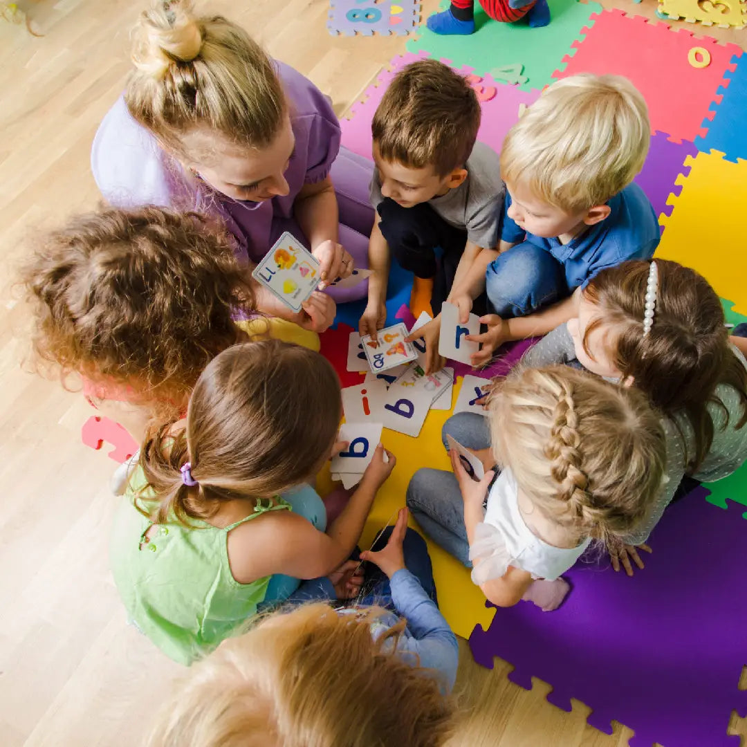 Children sitting on a colorful foam mat learning with alphabet cards.